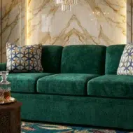 Luxury emerald green velvet rolled arm sofa with patterned cushions in elegant modern living room with marble wall and chandelier UAE
